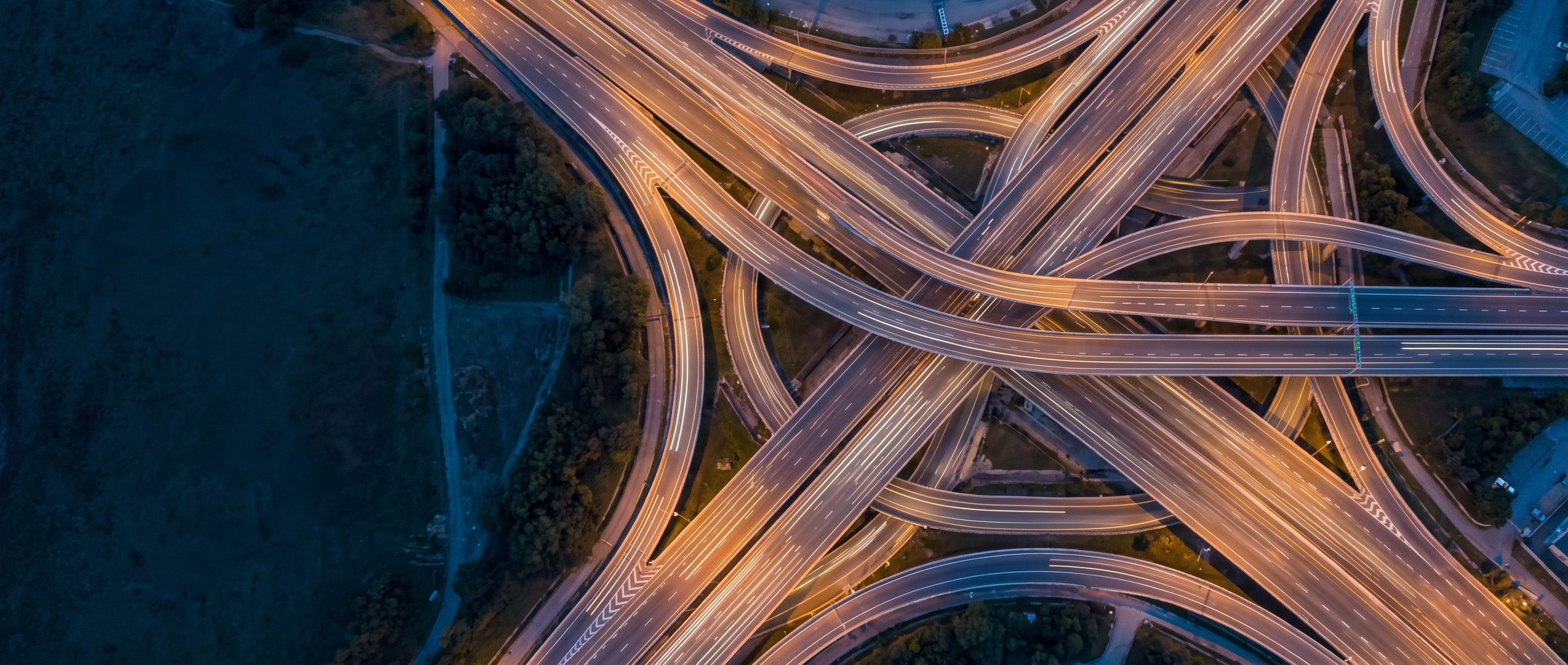 Svincolo autostradale visto dall'alto al crepuscolo, con le scie luminose del traffico