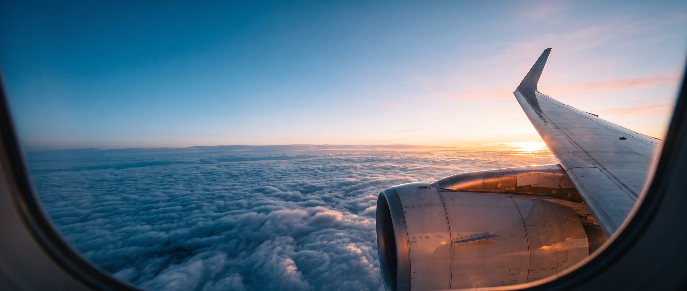 View from an aircraft window: wing and engine above a sea of clouds at sunset
